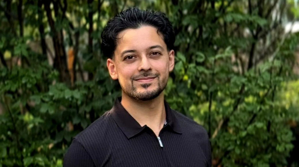 Sami Ahmed outside with green leaves in the background Sami Ahmed outside with green leaves in the background